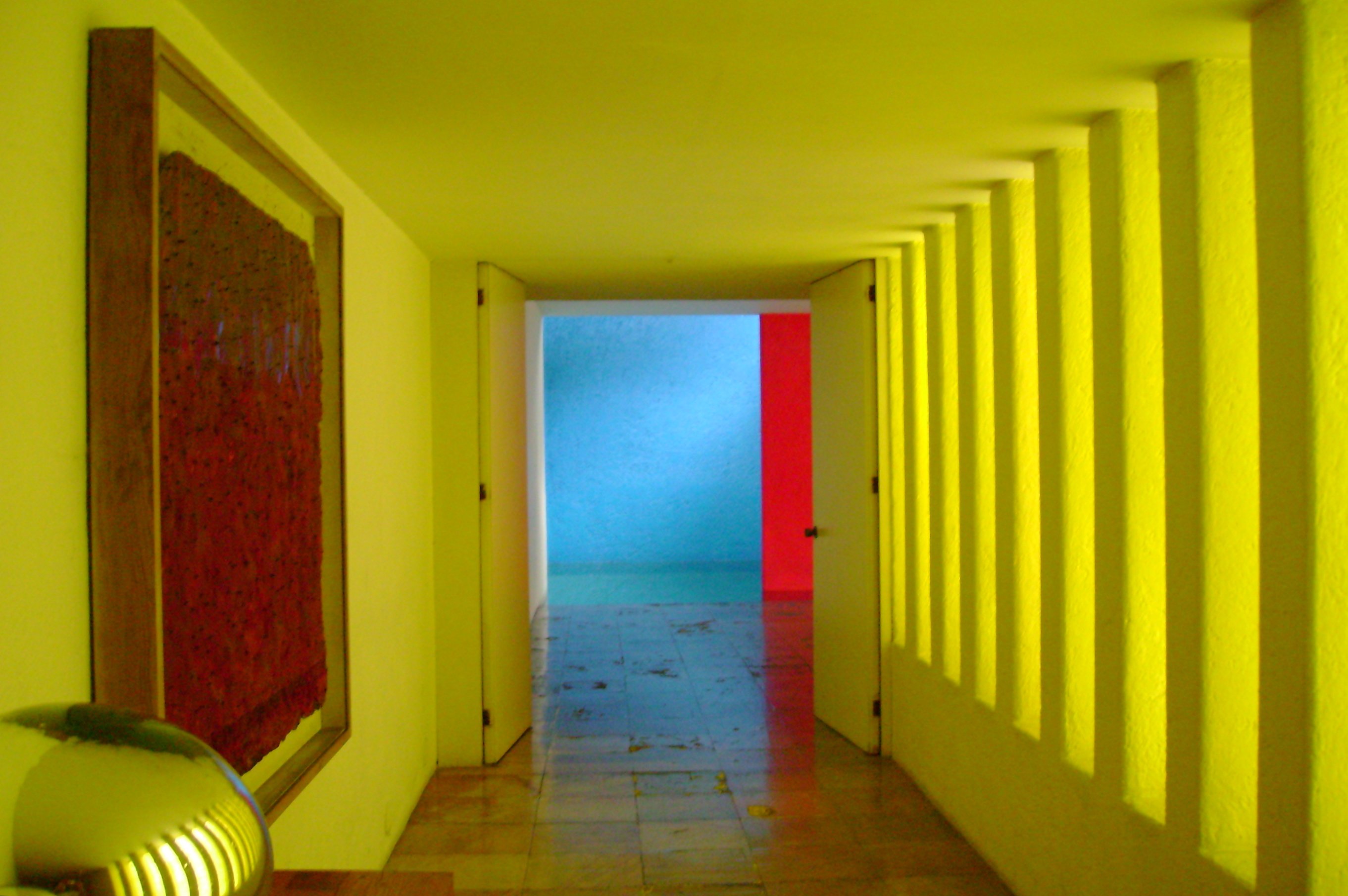 Interior corridor of Casa Gilardi by Luis Barragán, yellow hallway leading to a blue pool wall and magenta screen
